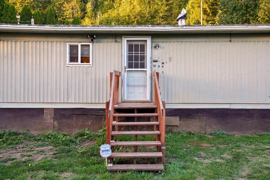 Exterior view of a mobile home with wooden steps on a sunny day.